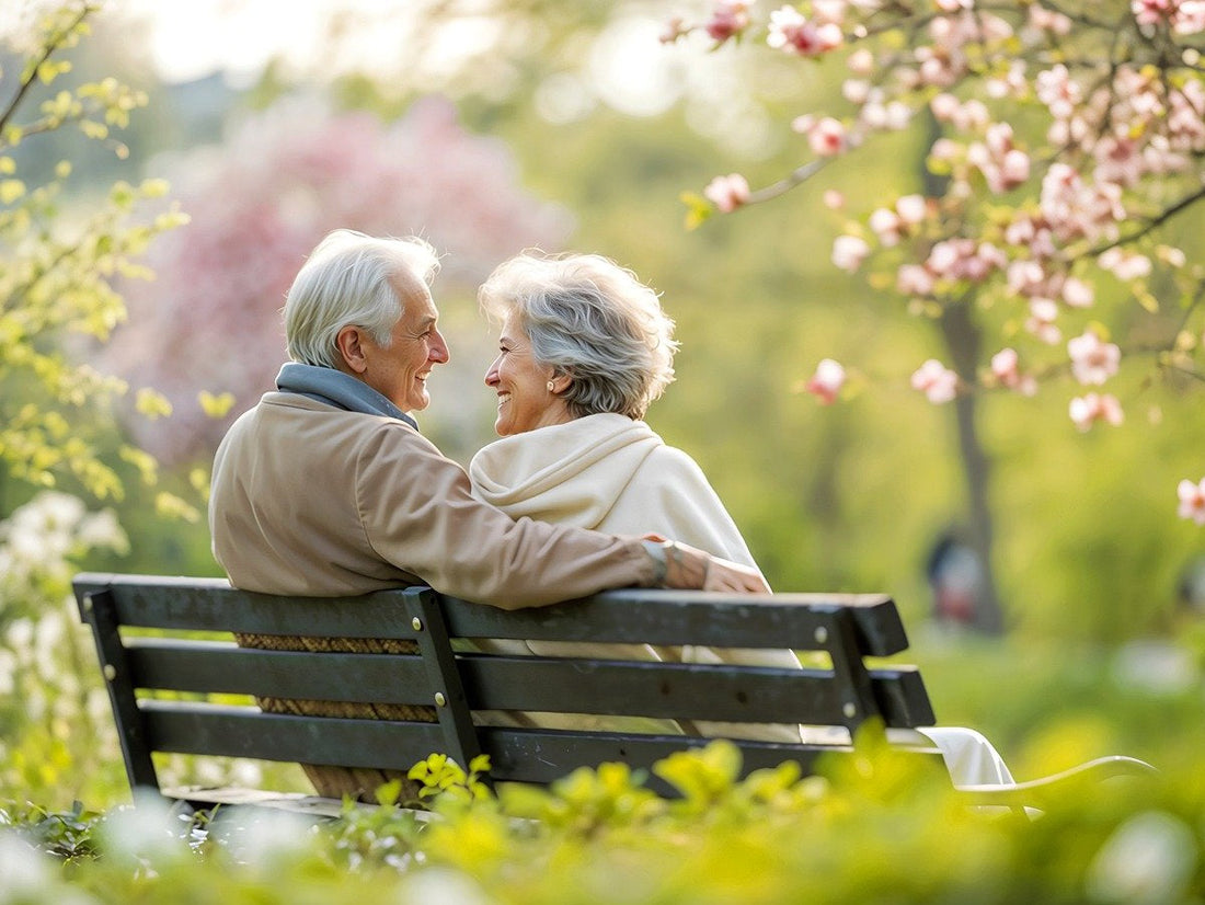 An elderly couple sat together on a park bench, smiling at each other.